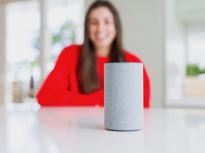 A voice operated smart home device on a table with a woman in the background.